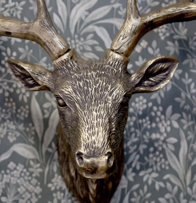 Bild av hjorthuvud i antik mässing mot blågrå botanisk tapet