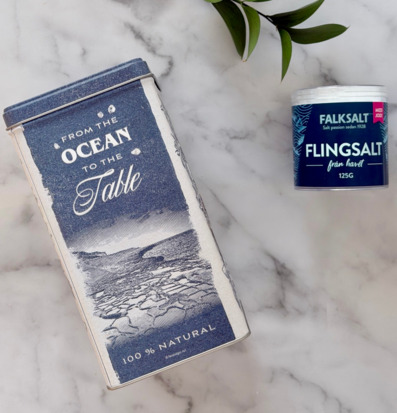 Bild med stilrena saltbehållare på marmoryta och gröna blad