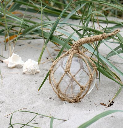 Foto: Glasflöte i repnät på sand med snäckor