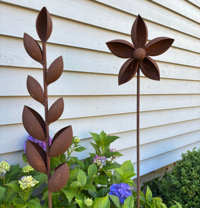 Foto: Rostiga metallstavar bland hortensior vid vägg