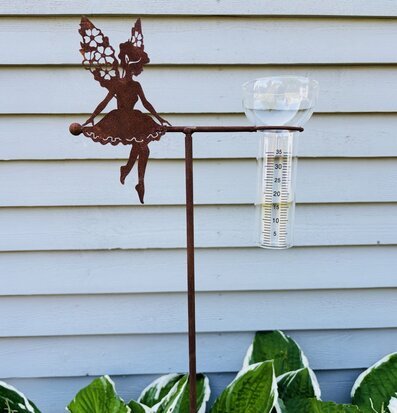 Bild på rostig älvfigur med regnmätare mot fasad