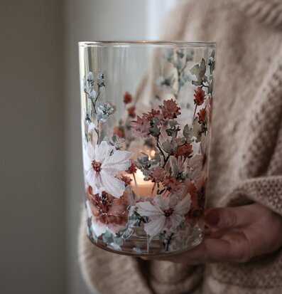 Foto av glaslykta med blomtryck och tänt ljus inne