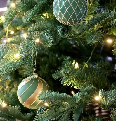 Foto: Olivgröna julkulor i guld på julgran nära ljus