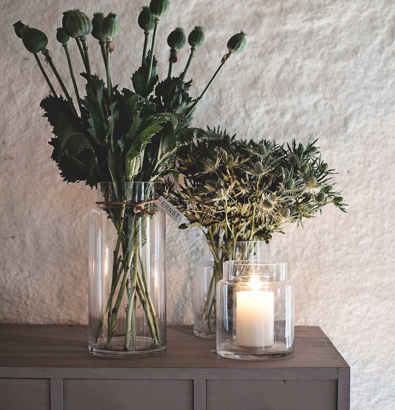 Glasvas ERNST från Ernst på grå byrå med blommor och ljus