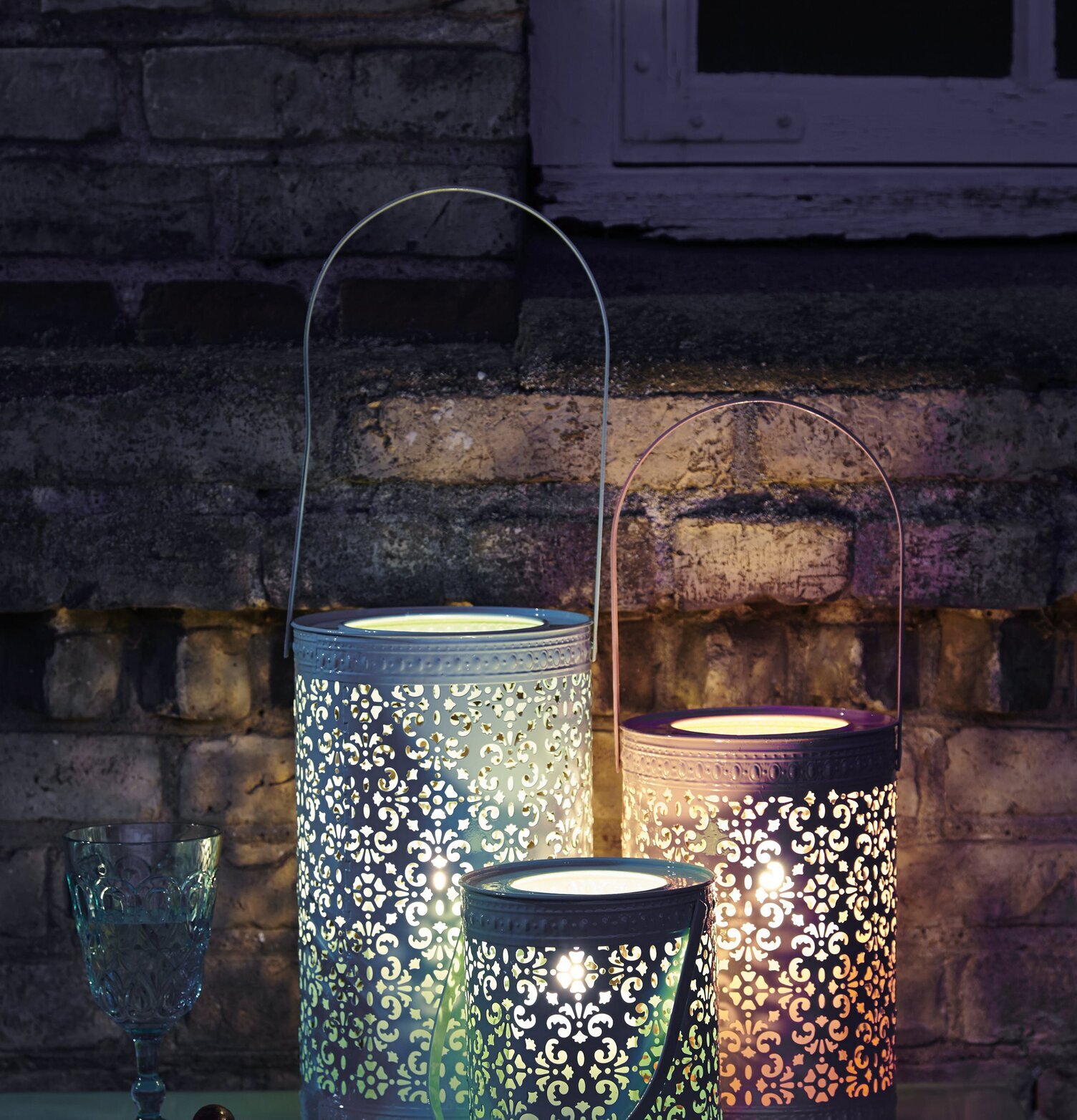 Lykta Garden Grön från Rice i trädgårdsmiljö med tegelvägg