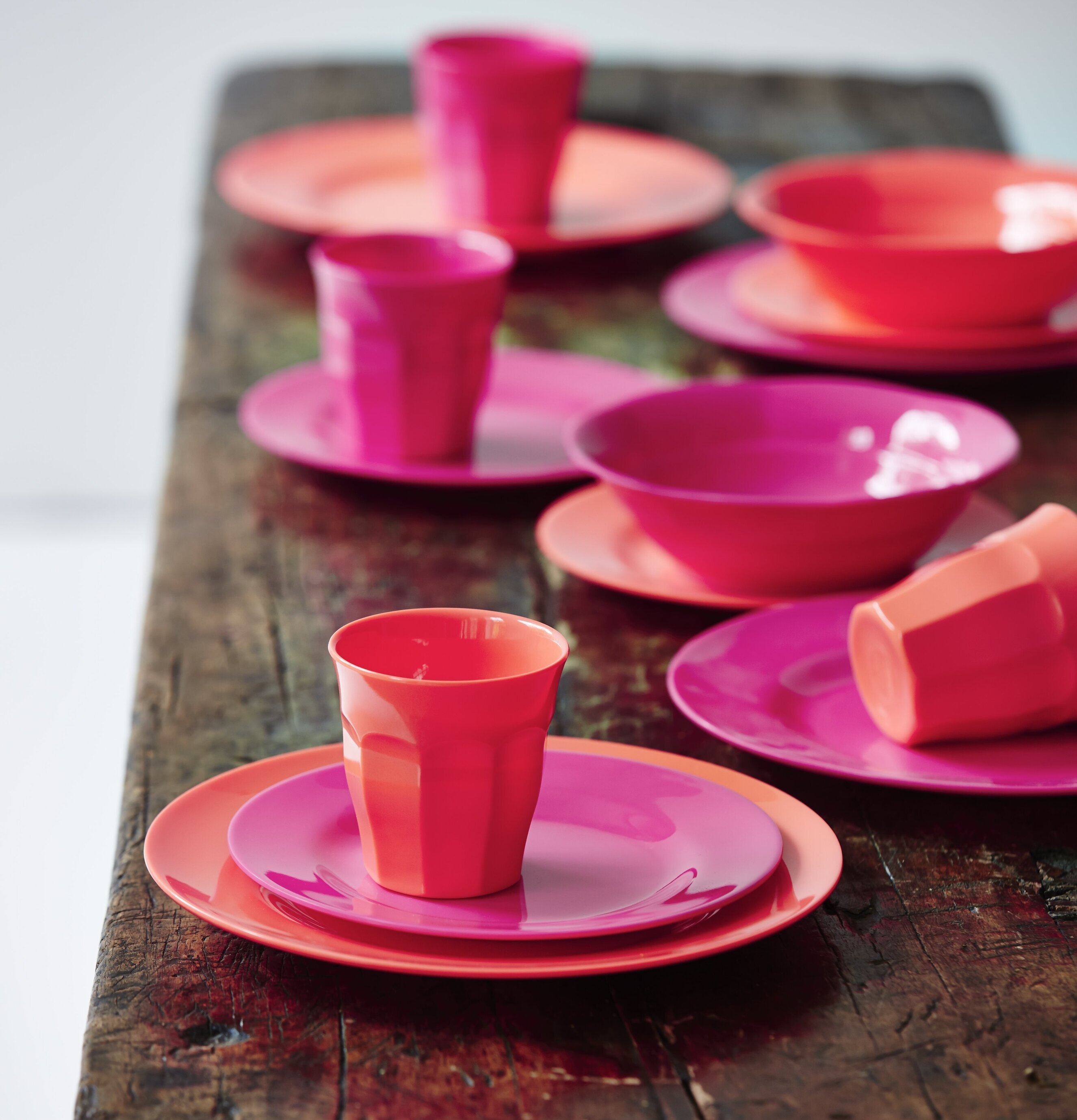 Assiett Neon Pink från Rice på rustikt träbord med färgglada koppar