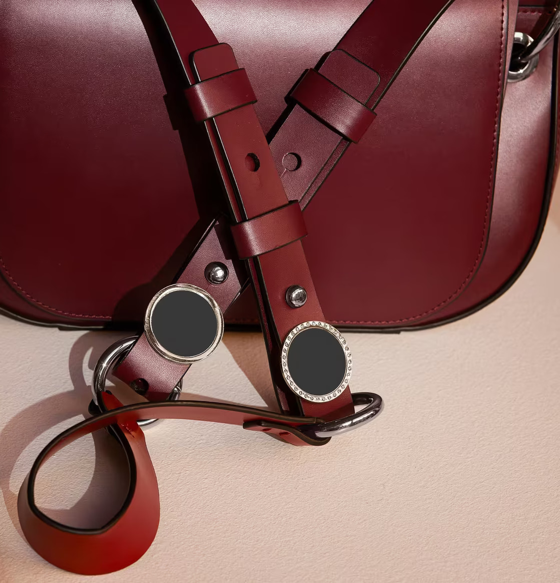 Reflexbrosch Silver från Firefly fäst på mörkröd läderväska