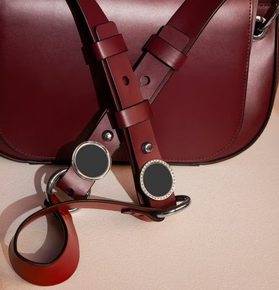 Reflexbrosch Silver från Firefly fäst på mörkröd läderväska